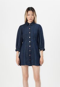 Denim skjortklänning med krage, knapp framtill och puffärmar. Mörkblått tyg med sydda detaljer och elastiska manschetter.