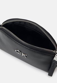 Pochette nera in pelle con zip e hardware argentato. Presenta un'esterno liscio, un branding minimale e una finitura testurizzata. L'interno è foderato.