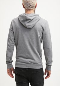 Sudadera con capucha gris con cordones en la capucha, mangas largas y puños acanalados. Textura suave, con un diseño sencillo y un ajuste relajado.