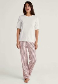 Vit kortärmad topp i kombination med rosa och vita randiga pyjamasbyxor. Tyget verkar mjukt och avslappnat, med en bekväm passform.