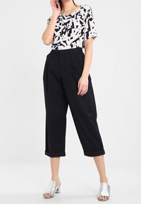 Top a maniche corte con un motivo astratto bianco e nero, abbinato a pantaloni cropped in blu navy a vita alta e sandali a scivolo argentati.