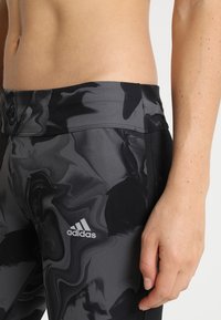 Black and gray marble-patterned leggings with a wide waistband, made of stretch fabric, featuring the Adidas logo on the front.