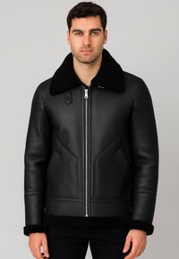 Chaqueta de cuero negro con cuello de borrego, con cremallera frontal, bolsillos laterales y puños y dobladillo texturizados en negro.