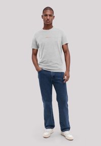 Heather gray cotton t-shirt with a round neck, featuring a small orange logo at the chest. Worn with blue denim jeans and white sneakers.