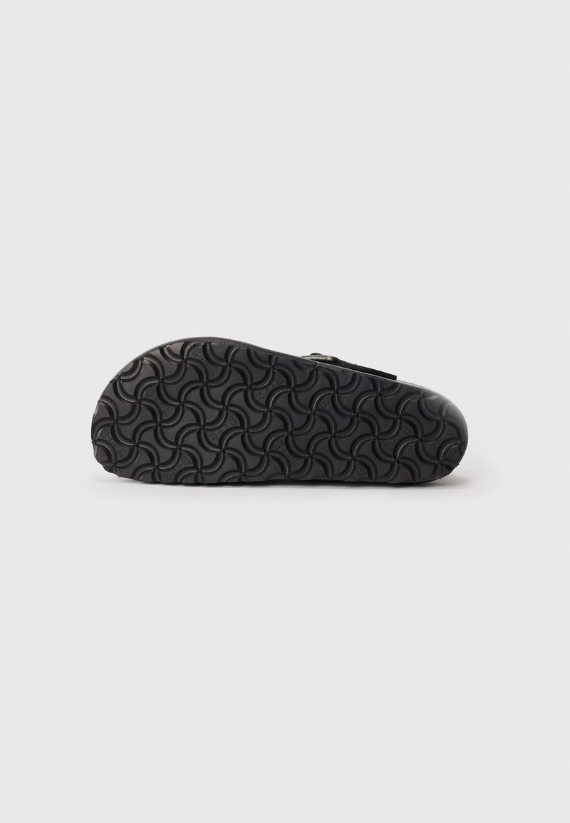 Black footwear with a textured rubber sole featuring a spiral pattern. The design includes a single strap and a contoured shape.