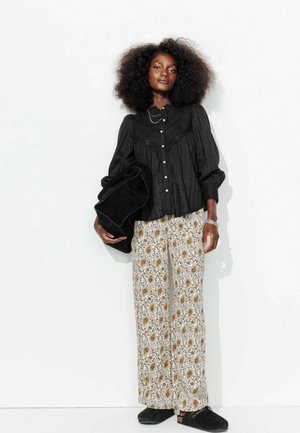Blouse noire avec des manches bouffantes et patte de boutonnage, associée à un pantalon ample à motif cachemire en blanc, jaune et noir. Chaussures à enfiler noires.