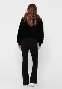 Czarny polarowy sweter o skróconym kroju, w zestawieniu z czarnymi spodniami typu dzwony. Materiał ma fakturowane wykończenie. Białe sneakersy dopełniają stylizację.
