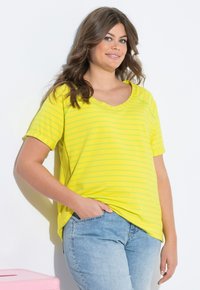 T-shirt jaune à rayures avec un col en V et des manches courtes, fabriqué en tissu doux. Associé à un jean en denim bleu clair. Design simple et décontracté.