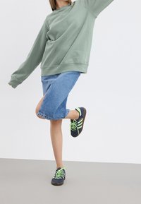 Groene oversized sweater, blauwe denim rok met zijsplit, en zwarte sneakers met groene veters. Minimalistisch ontwerp, casual pasvorm.