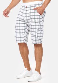 Shorts cargo à carreaux blancs avec des lignes vertes, dotés de plusieurs poches, d'une fermeture à bouton et d'une taille élastique pour le confort.