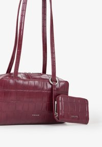 Borsa bordeaux in finta pelle di coccodrillo con due manici, chiusura zip e un portafoglio abbinato removibile, caratterizzata da una superficie texturizzata e lucida.
