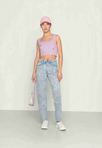 Top cropped de malha lilás com pequenos detalhes bordados, jeans de patchwork azul claro de cintura alta, ténis brancos e uma capa rosa claro.