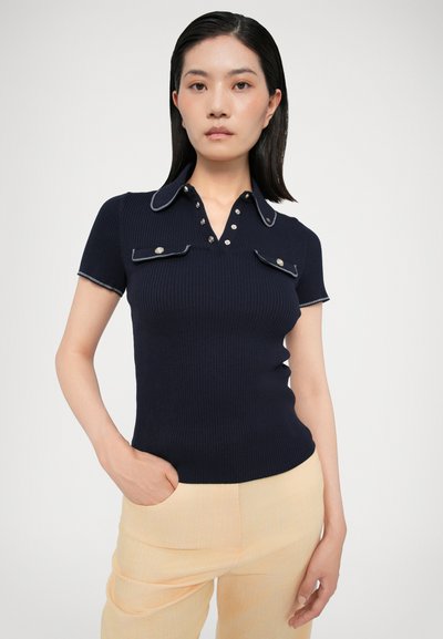 Navy ribbed polo shirt with short sleeves, contrasting white collar and button detail, paired with light yellow textured trousers.
