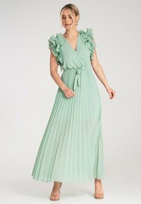 Jasnozielona długa sukienka z plisowanym materiałem, falbaniastymi krótkimi rękawami, dekoltem w kształcie litery V oraz wiązaniem w talii. Gładka, płynąca tekstura.