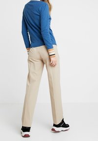 Blå ribbad långärmad topp med vitt krage och flerfärgade manschetter, ihop med beige högmidjade byxor och svarta träningsskor.