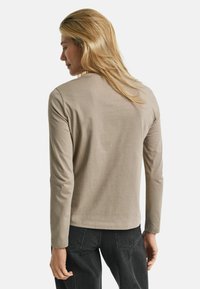 Langärmliges Hemd aus leichtem beigen Baumwollstoff, taillierter Schnitt mit rundem Ausschnitt, glatte Textur und minimale Nähte.