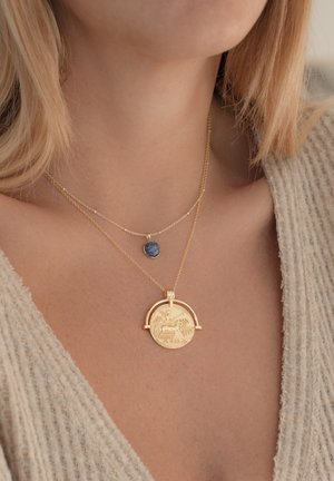 Goldene Halskette mit einem runden Anhänger, der aufwendige Details aufweist, und einem kleineren blauen Steinanhänger, der darüber geschichtet ist. Vertikale Ketten.
