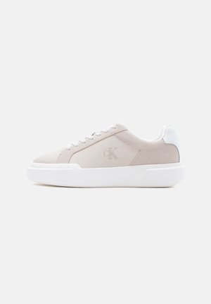 Beige lage sneaker met dikke witte zool, veters en hielstuk, met subtiel "cK"-logo op het zijpaneel.