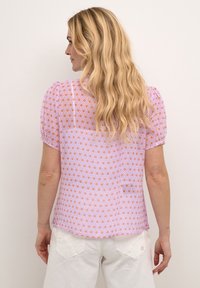 Lila Kurzarmbluse mit einem Diamantmuster in Orange und Pink. Leichtes Material mit rundem Rückenausschnitt und subtiler Textur.