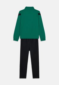 Groene lange mouwen top met een kraag en zwarte schouderstrepen, gecombineerd met zwarte broek. De stof lijkt glad met een getailleerd ontwerp.