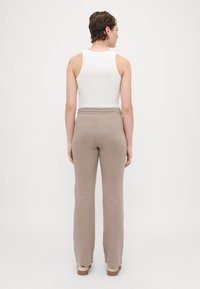 Pantaloni de trening bej cu talie elastică striată și croială dreaptă, asortați cu un tricou fără mâneci alb, priviți din spate.