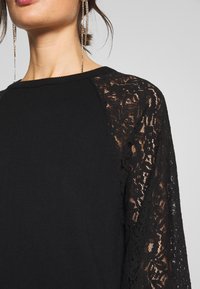 Zwart topje met lange mouwen en ingewikkeld kantwerk op de schouders en een effen lichaam, gemaakt van een zachte textielstof.