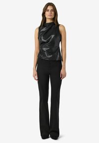 Crna majica bez rukava s naboranom teksturom, izrađena od sjajnog materijala; uparena s crnim širim hlačama za usklađen izgled.
