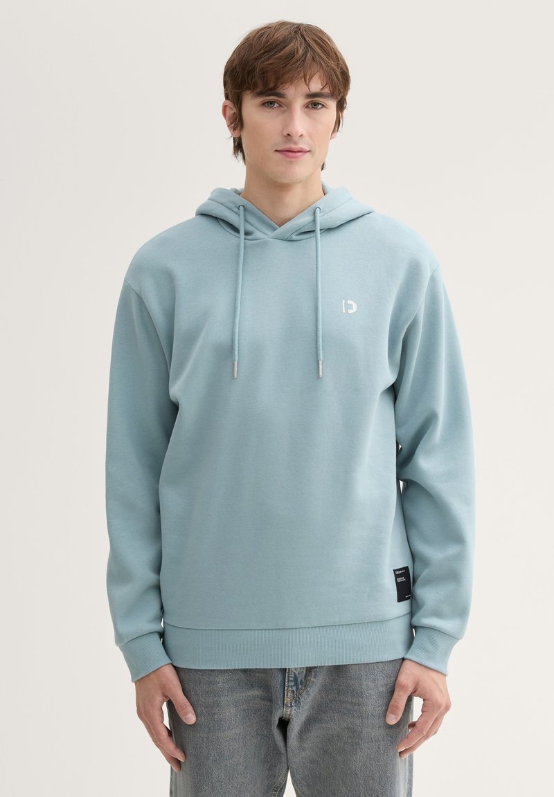 Felpa blu chiaro con tasca frontale, cordini regolabili e polsini a coste. Presenta un piccolo logo sul petto e un'etichetta in tessuto all'orlo.