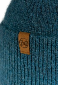 Gorro de punto azul con textura acanalada, que presenta una etiqueta de cuero marrón con logo grabado. Hilo suave y grueso para calidez y comodidad.