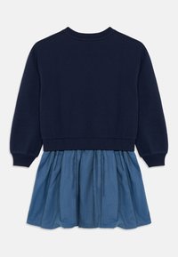 Tengerészkék pulóver hosszú ujjakkal, világoskék farmer szoknyával párosítva, amely hullámokkal díszített derékrészen és sima textúrával rendelkezik.