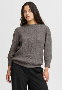 Pull en maille gris à col rond et manches trois-quarts, fabriqué en tissu mélange de laine texturé. Associé à un pantalon noir.