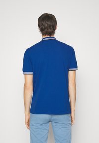 Blå pikétröja med en klassisk design, med korta ärmar, kontrasterande randsydd krage och en mjuk struktur.