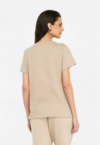 T-shirt beige à manches courtes, en coton doux, design classique à col rond, coupe décontractée, texture unie, porté avec un pantalon beige assorti.