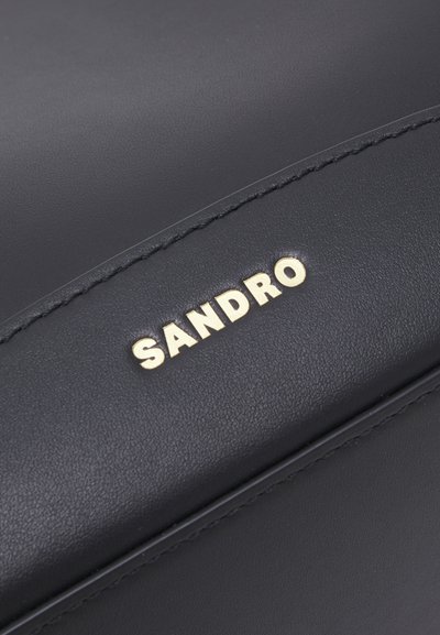 Borsa in pelle nera con logo "SANDRO" in oro embossato, texture liscia e cuciture a contrasto. Design minimalista con forma rettangolare.