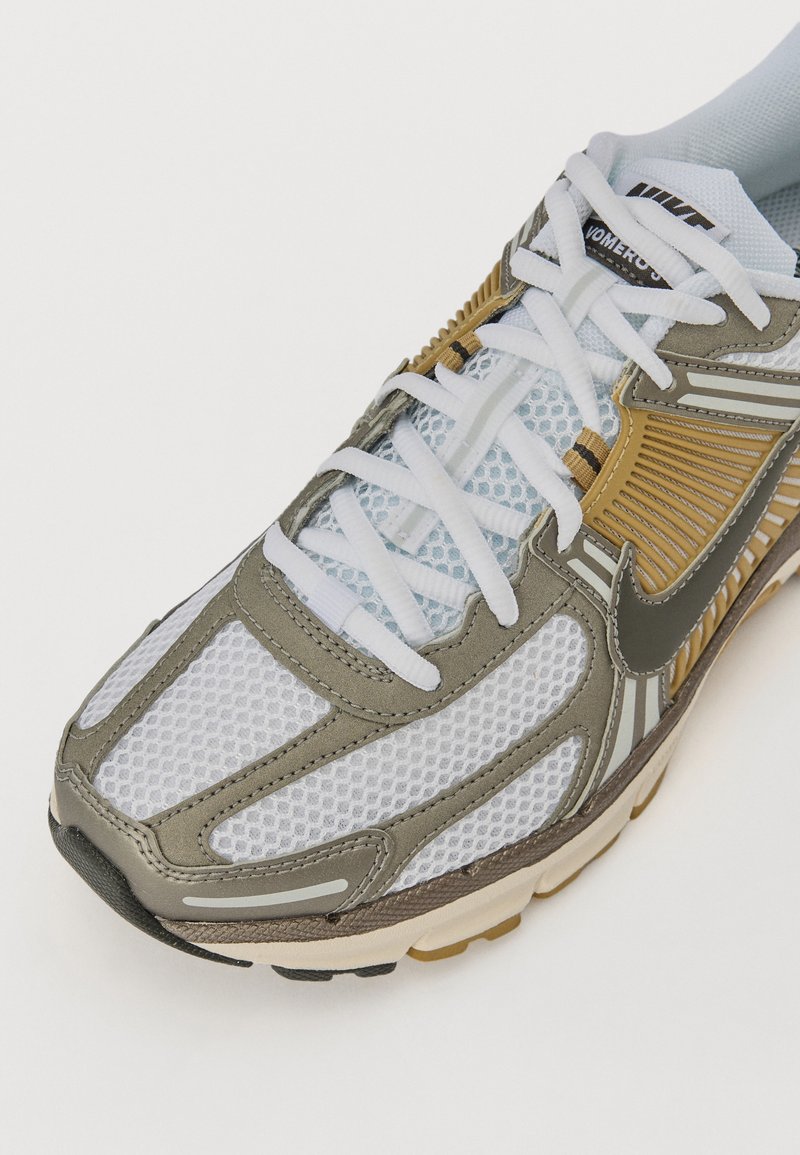 Nike Laufschuhe mit einem hellgrauen Netz-Obermaterial, verstärkt durch olivgrüne Akzente und silberne Details, mit weißen Schnürsenkeln und einer gepolsterten Sohle.