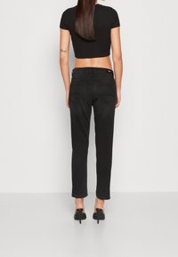 Svarta högmidjade jeans med slim fit, som har bakfickor och en slät denimtextur, i kombination med en kort svart topp.