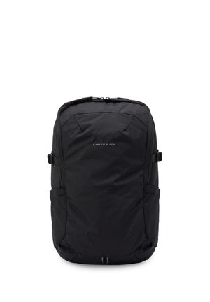 Black Kapten & Son backpack with a minimalist design, front zippered pocket, and side straps for adjustment.