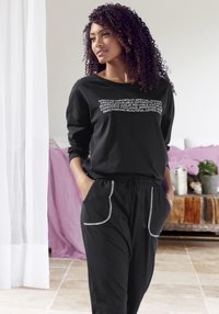 Black long-sleeve top with white text, paired with black pants featuring white side stitching and pockets. Soft material and relaxed fit.