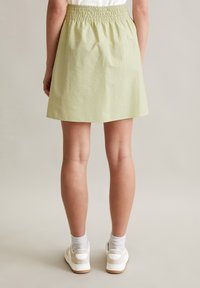 Een lichtgroene, knielange rok met een gerimpelde tailleband, gemaakt van een gestructureerde stof, in combinatie met witte sneakers en grijze sokken.