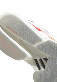 Tenisky s bílou gumovou podrážkou s texturovaným vzorem, oranžovými akcenty a brandingovými prvky včetně "LIGHTTRAXION" a "ADIZERO."