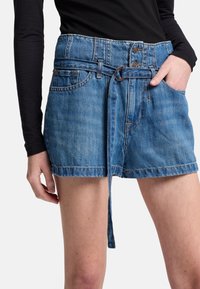 Shorts in denim di colore azzurro chiaro con cintura annodata in vita, chiusura a bottone e quattro tasche. Presentano un orlo leggermente sfrangiato e dettagli cuciti.
