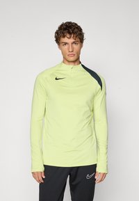 Koszula z długim rękawem i wysokim kołnierzem w jaskrawym żółtym kolorze, z ciemnozielonymi akcentami na ramionach oraz logo Nike na piersi. Gładki, sportowy krój.