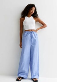 Pantalon large à rayures bleu clair avec taille à cordon de serrage ; associé à un top ajusté blanc et des sandales noires. Texture lisse.