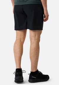 Svarta atletiska shorts med en slät yta och en lös passform, tillsammans med svarta löparskor med en texturerad sula och snörning.