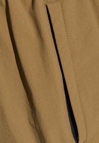 Beige stof met een zachte textuur, met een zwart ritsdetail langs de naad. Gestikte randen zijn zichtbaar, wat de structurele integriteit versterkt.