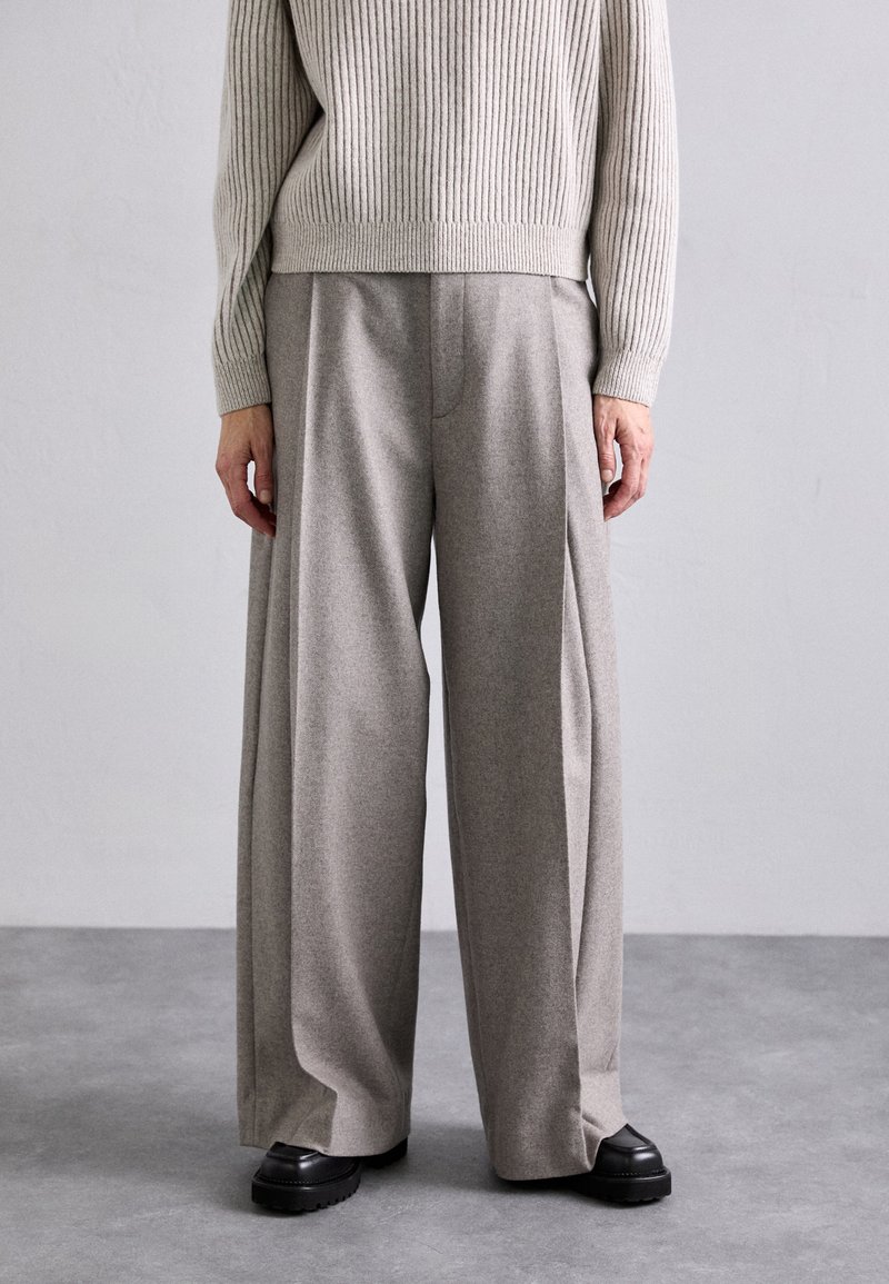 Wide-legged trousers in light gray fabric with a soft texture, featuring front pleats and a smooth waistband, paired with black platform shoes.