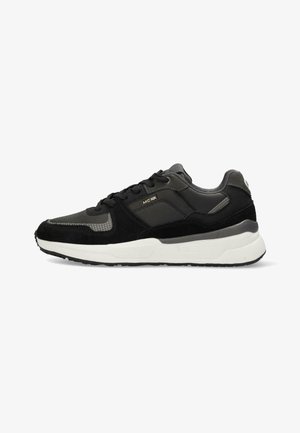 Sneaker nera con materiali sintetici e scamosciati, superfici testurizzate, intersuola bianca, accenti grigi, lacci rotondi e un logo sul lato.