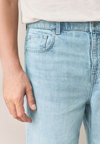 Jeans in denim azzurro chiaro con un design classico a cinque tasche, vestibilità regolare e leggero effetto scolorito. Cuciture ricamate e chiusura con bottone visibili.