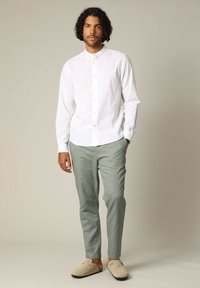 Witte blouse met lange mouwen en een Mandarin-kraag, gecombineerd met lichtgroene slim-fit broek en beige instappers.