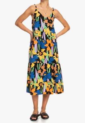 Femme portant une robe sans manches à col en V, de longueur midi, avec un grand motif floral coloré en bleu, jaune, orange, vert et violet.